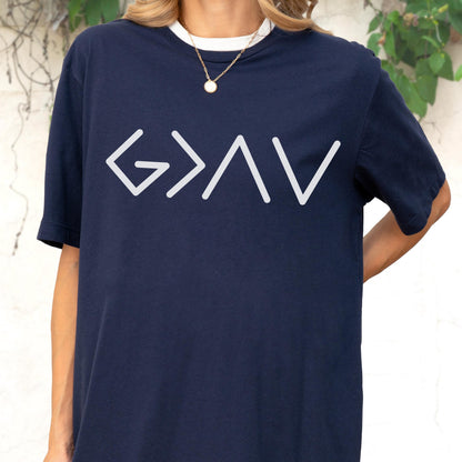 May include: A navy blue short-sleeved t-shirt featuring a white graphic print on the chest. The design consists of the mathematical symbols G > I V, which represent the phrase God is greater than the highs and lows. The shirt has a crew neckline.