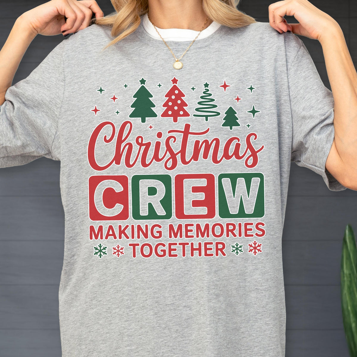 May include: A heather gray t-shirt featuring a festive graphic with four stylized Christmas trees and stars above the red script text Christmas and the block letters CREW in red and green boxes, followed by the text MAKING MEMORIES TOGETHER.