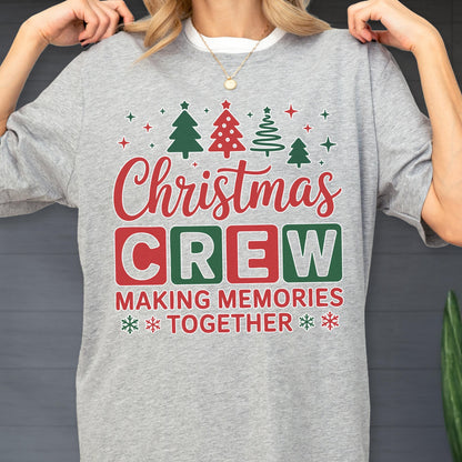 May include: A heather gray t-shirt featuring a festive graphic with four stylized Christmas trees and stars above the red script text Christmas and the block letters CREW in red and green boxes, followed by the text MAKING MEMORIES TOGETHER.