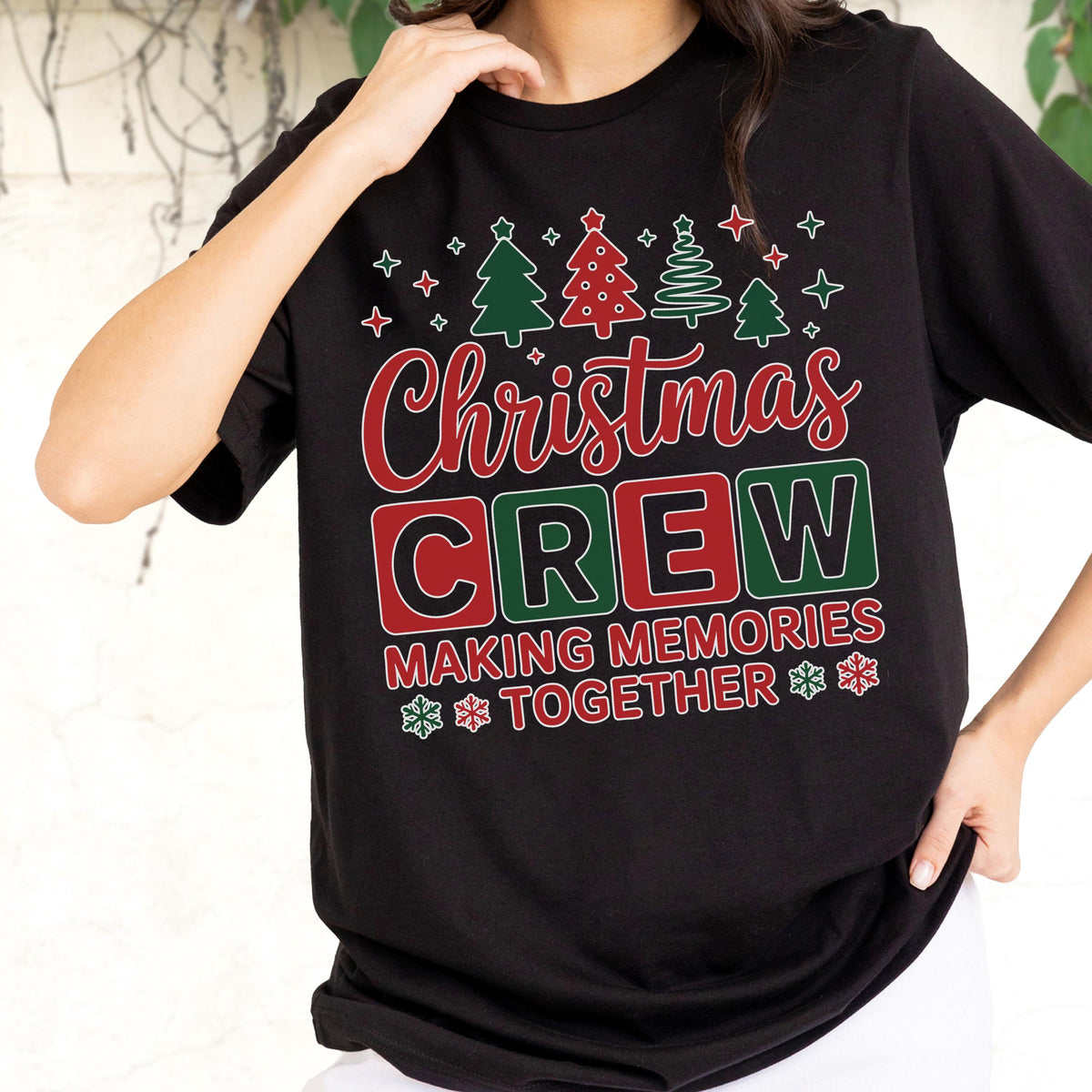 May include: A black t-shirt featuring a graphic design with red and green Christmas trees at the top. The text reads Christmas CREW in red and green, followed by MAKING MEMORIES TOGETHER in red, accented with small white snowflakes and stars.