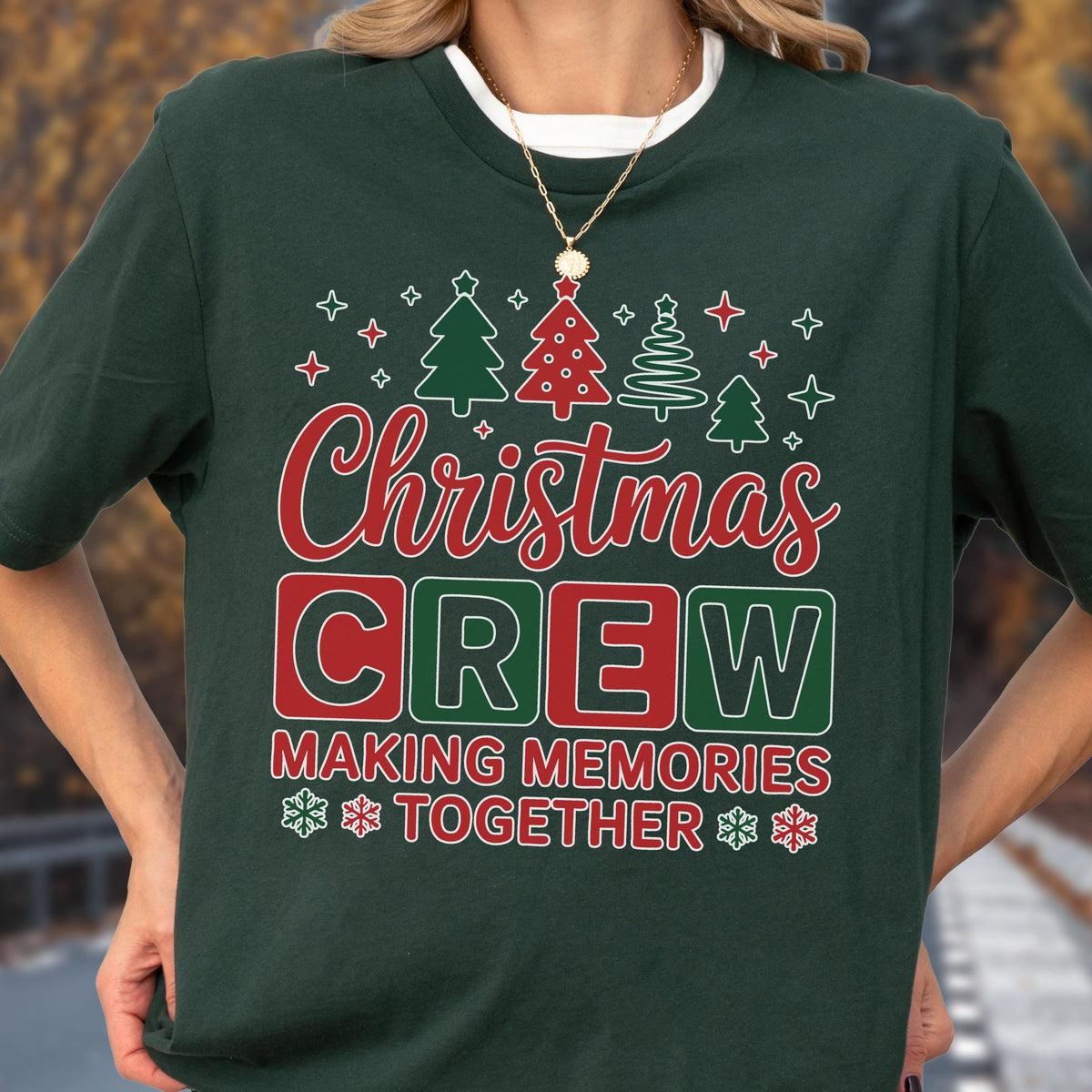 May include: A dark green t-shirt featuring a graphic with the text "Christmas CREW MAKING MEMORIES TOGETHER" in red and white. The design includes illustrations of four stylized Christmas trees and small snowflakes in red and white colors.