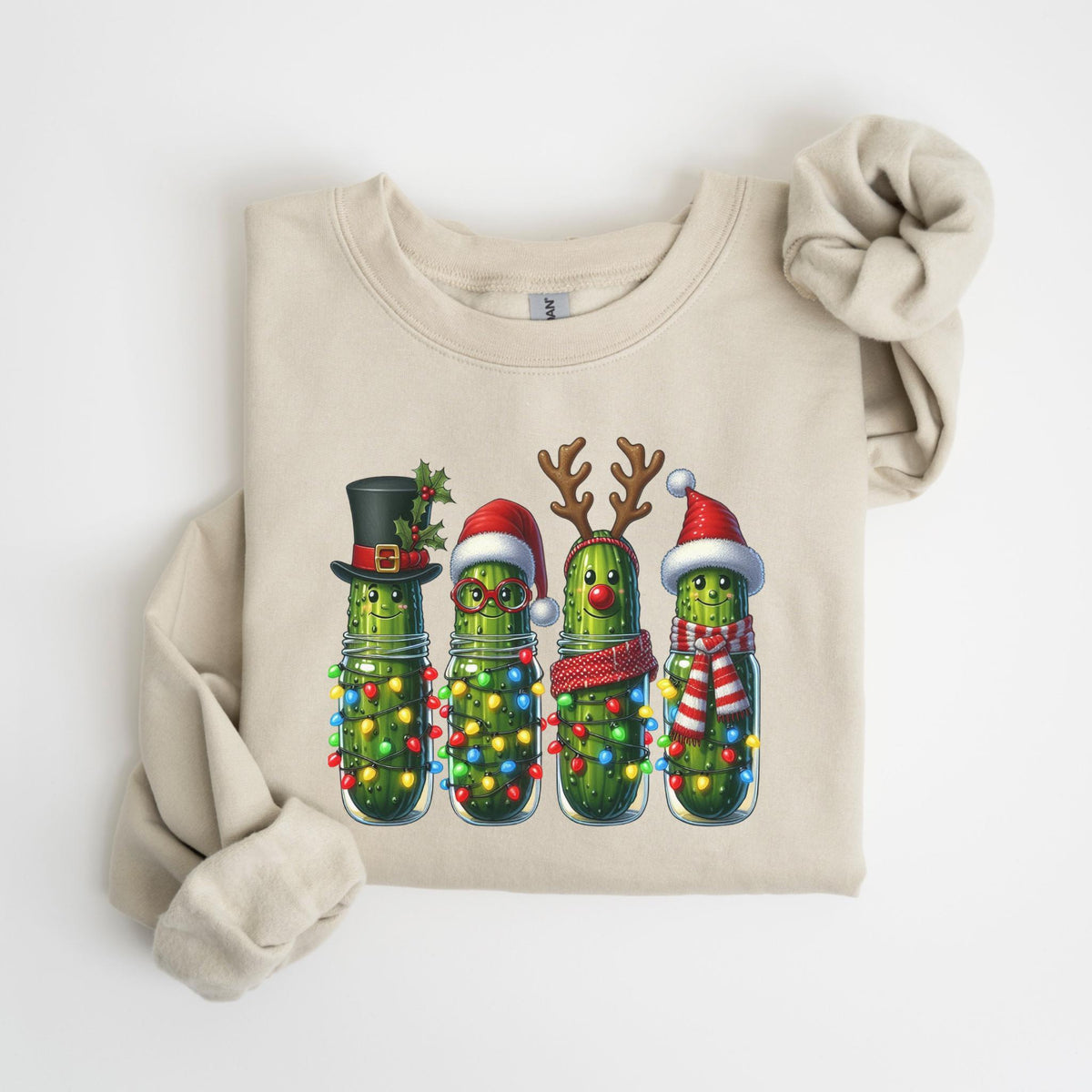 May include: A beige sweatshirt features a festive graphic of four anthropomorphic pickles in glass jars, each adorned with holiday accessories. One wears a top hat, another glasses and a Santa hat, the third reindeer antlers, and the last a Santa hat and scarf.