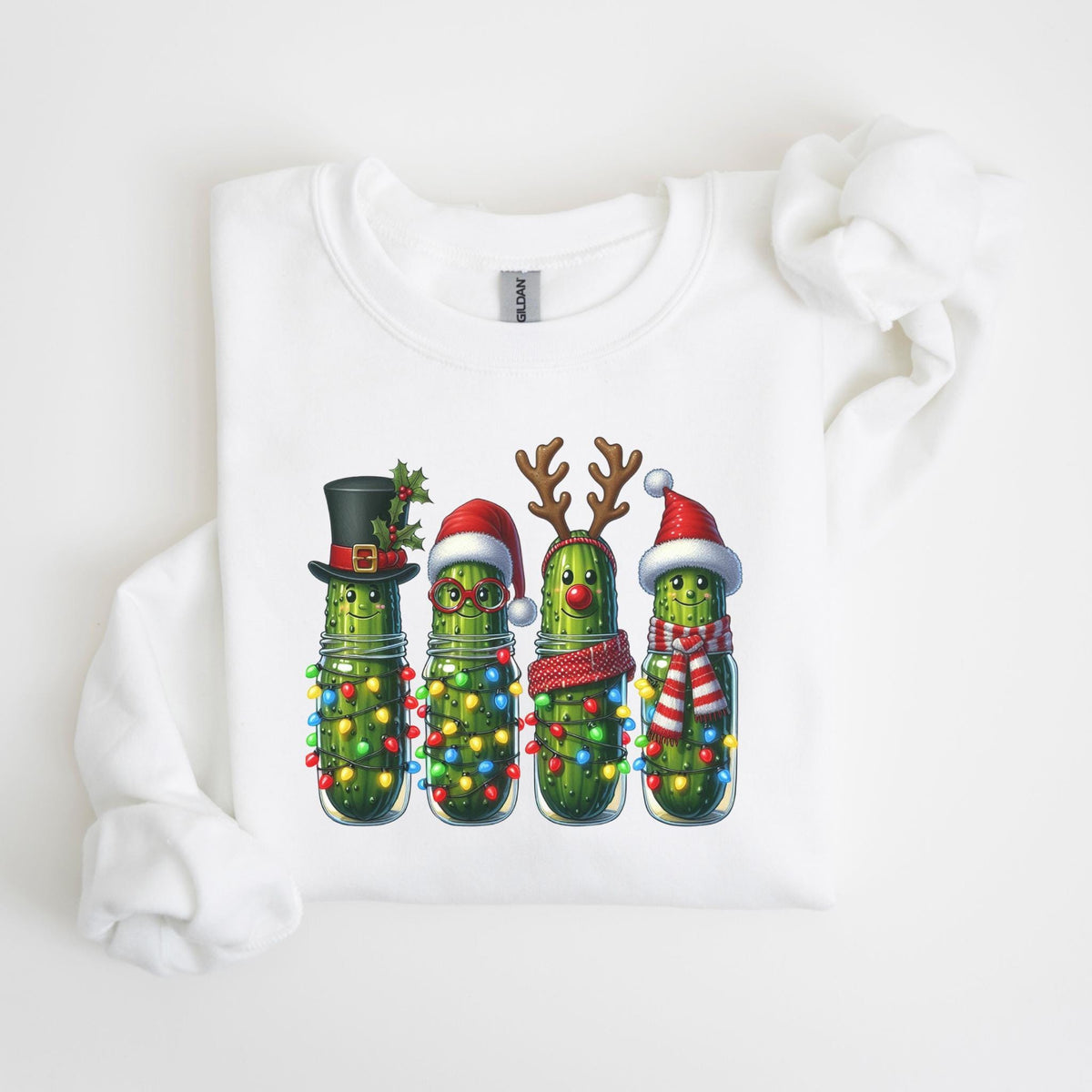 May include: White sweatshirt featuring a festive graphic of four anthropomorphic pickles in glass jars, each adorned with holiday accessories like a top hat, Santa hat, reindeer antlers, and a scarf. The pickles are decorated with colorful Christmas lights.