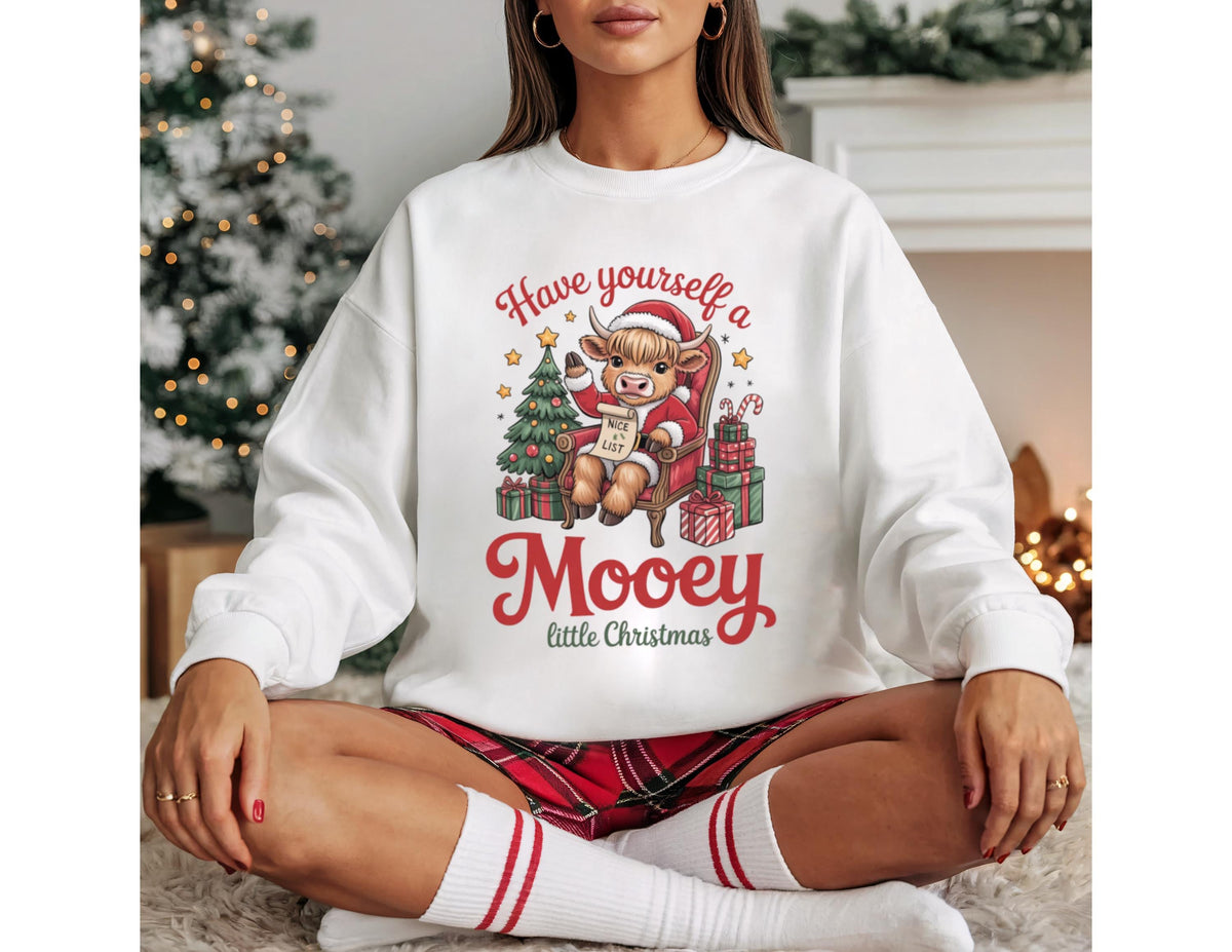 May include: White sweatshirt with a festive graphic. The design features a cartoon cow in a Santa hat, seated in a chair, with a Christmas tree and presents. Text reads "Have yourself a Mooey little Christmas."