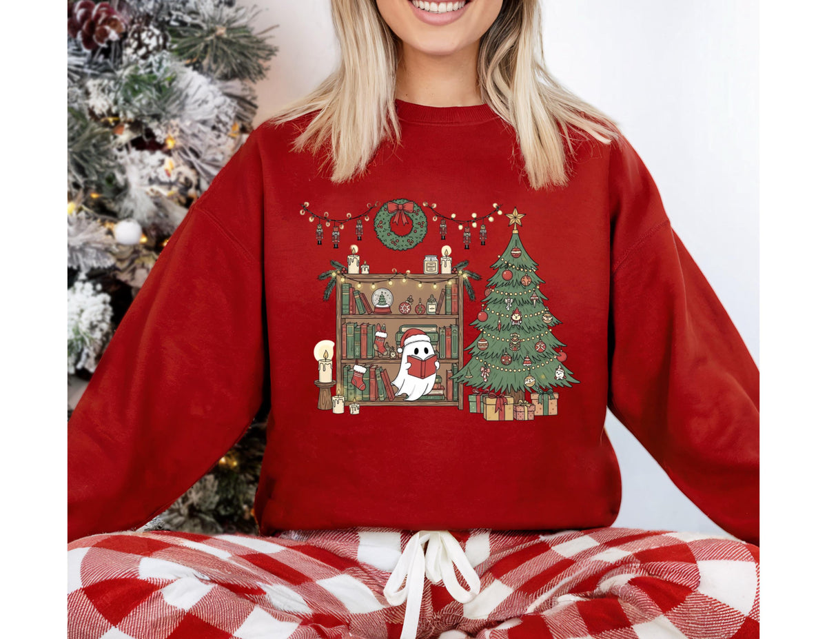 May include: A red sweatshirt featuring a Christmas-themed graphic. The graphic includes a Christmas tree, a bookshelf with candles, and a ghost reading a book. The sweatshirt is paired with red and white plaid pajama pants.