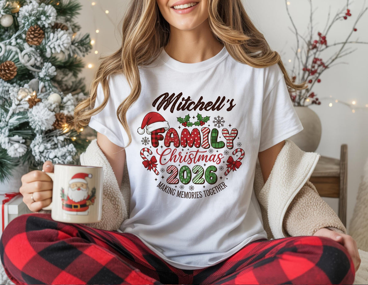 May include: White t-shirt with the text "Mitchell's Family Christmas 2026" in a festive design. The design includes a Santa hat, holly, snowflakes, and candy canes. The shirt is paired with red and black plaid pajama pants.