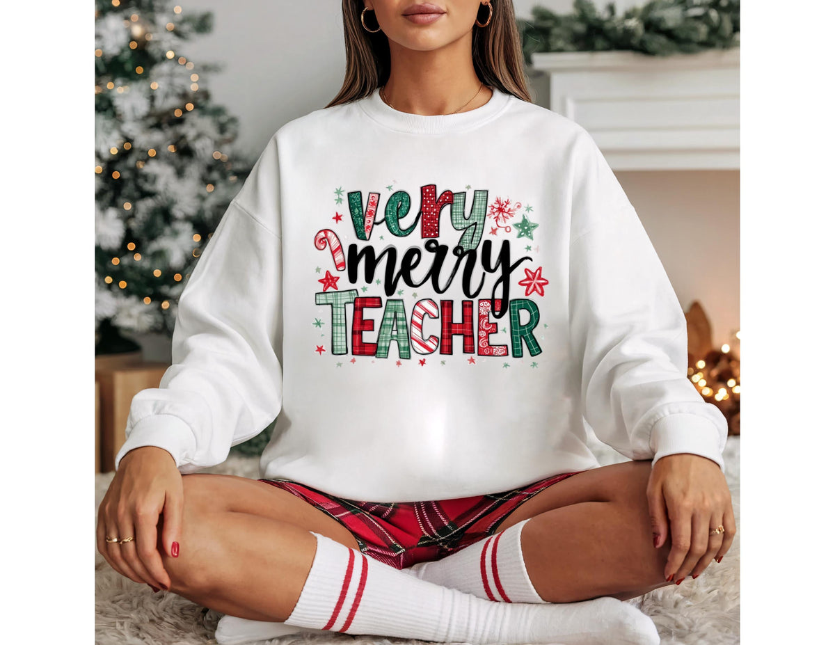 May include: White sweatshirt with the text "Very Merry Teacher" in a festive design. The text features red, green, and white colors with candy cane and snowflake accents. The sweatshirt is paired with red plaid shorts and white socks.