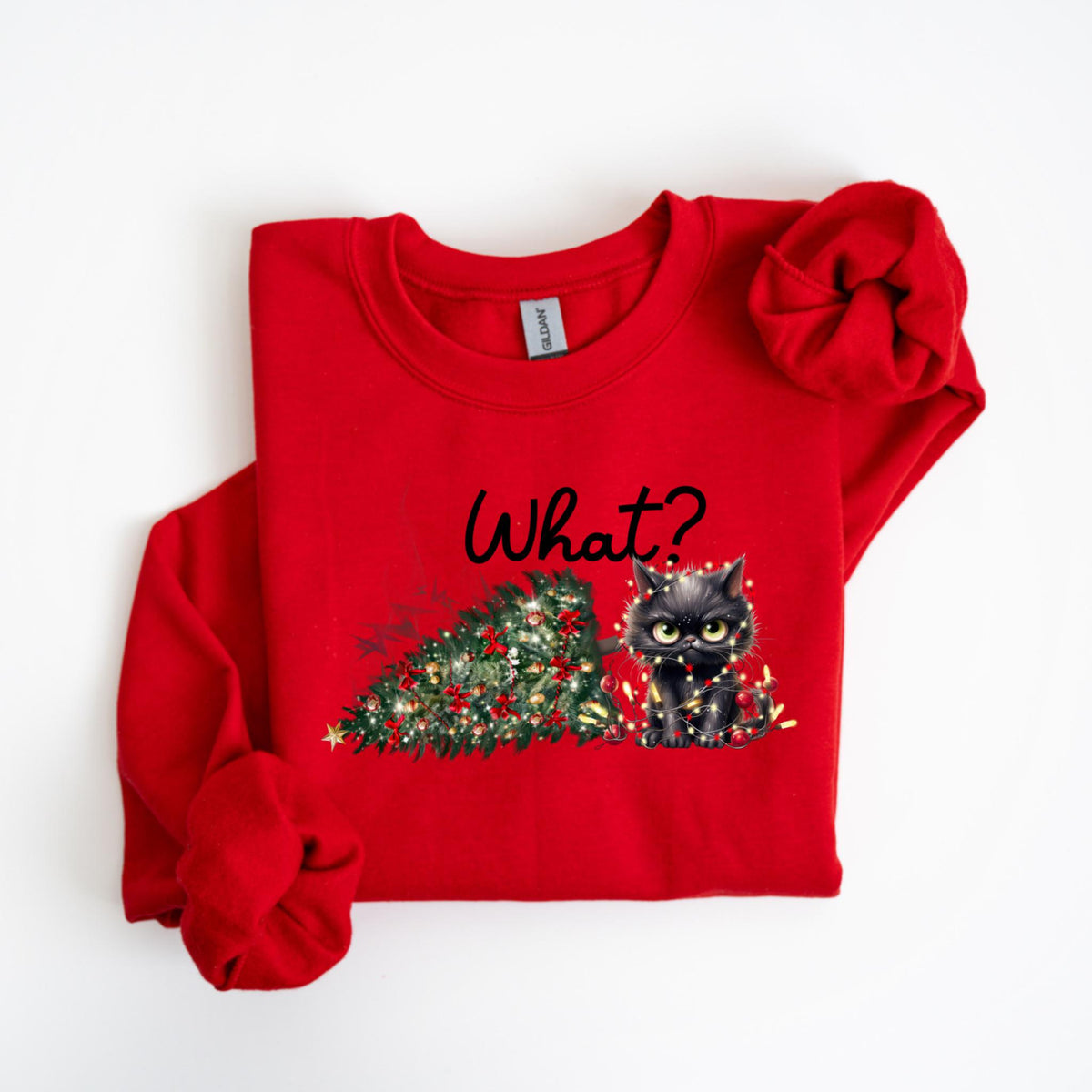 May include: A red sweatshirt featuring a black cat with yellow eyes, wrapped in Christmas lights, and a decorated Christmas tree. The word "What?" is written in black script above the cat and tree.
