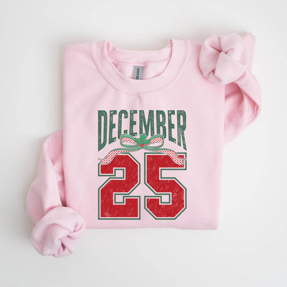 May include: A light pink sweatshirt with the text "DECEMBER 25" in green and red. The text has a distressed, vintage look, with a decorative bow above the number 25. The sweatshirt is a crew neck style.