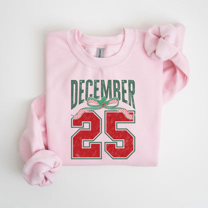 May include: A light pink sweatshirt with the text "DECEMBER 25" in green and red. The text has a distressed, vintage look, with a decorative bow above the number 25. The sweatshirt is a crew neck style.