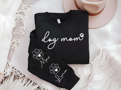 May include: Black sweatshirt with the words "dog mom" in white script and a paw print. The sleeve features paw prints with the names "Max" and "Luna". A neutral-colored hat rests in the background.