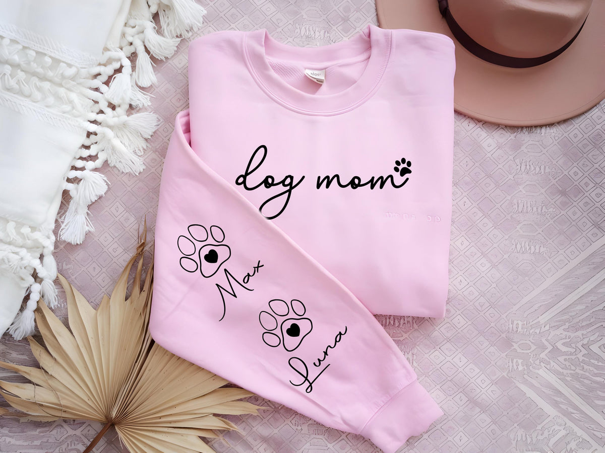 May include: A light pink sweatshirt with the words "dog mom" in black script and a paw print. The sleeve features paw prints with the names "Max" and "Luna".