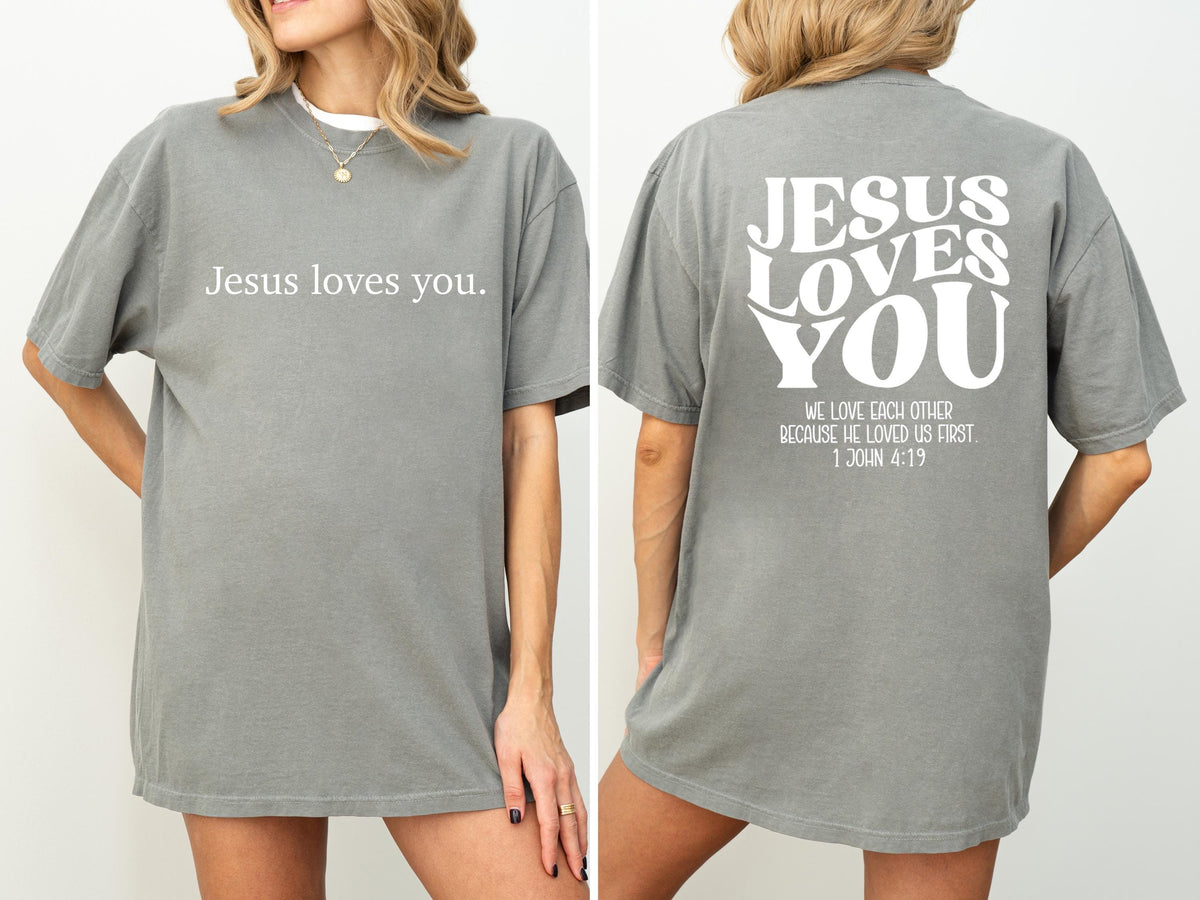 May include: Gray short-sleeved t-shirt with the text "Jesus loves you" on the front. The back of the shirt features the words "JESUS LOVES YOU" in a stylized font, along with a Bible verse.