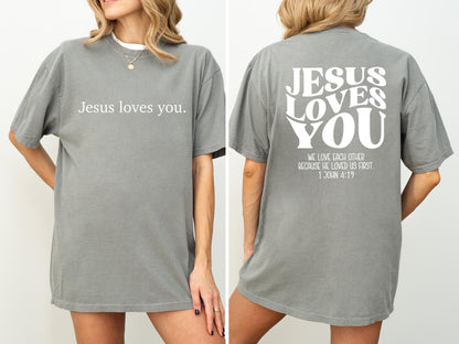 May include: Gray short-sleeved t-shirt with the text "Jesus loves you" on the front. The back of the shirt features the words "JESUS LOVES YOU" in a stylized font, along with a Bible verse.