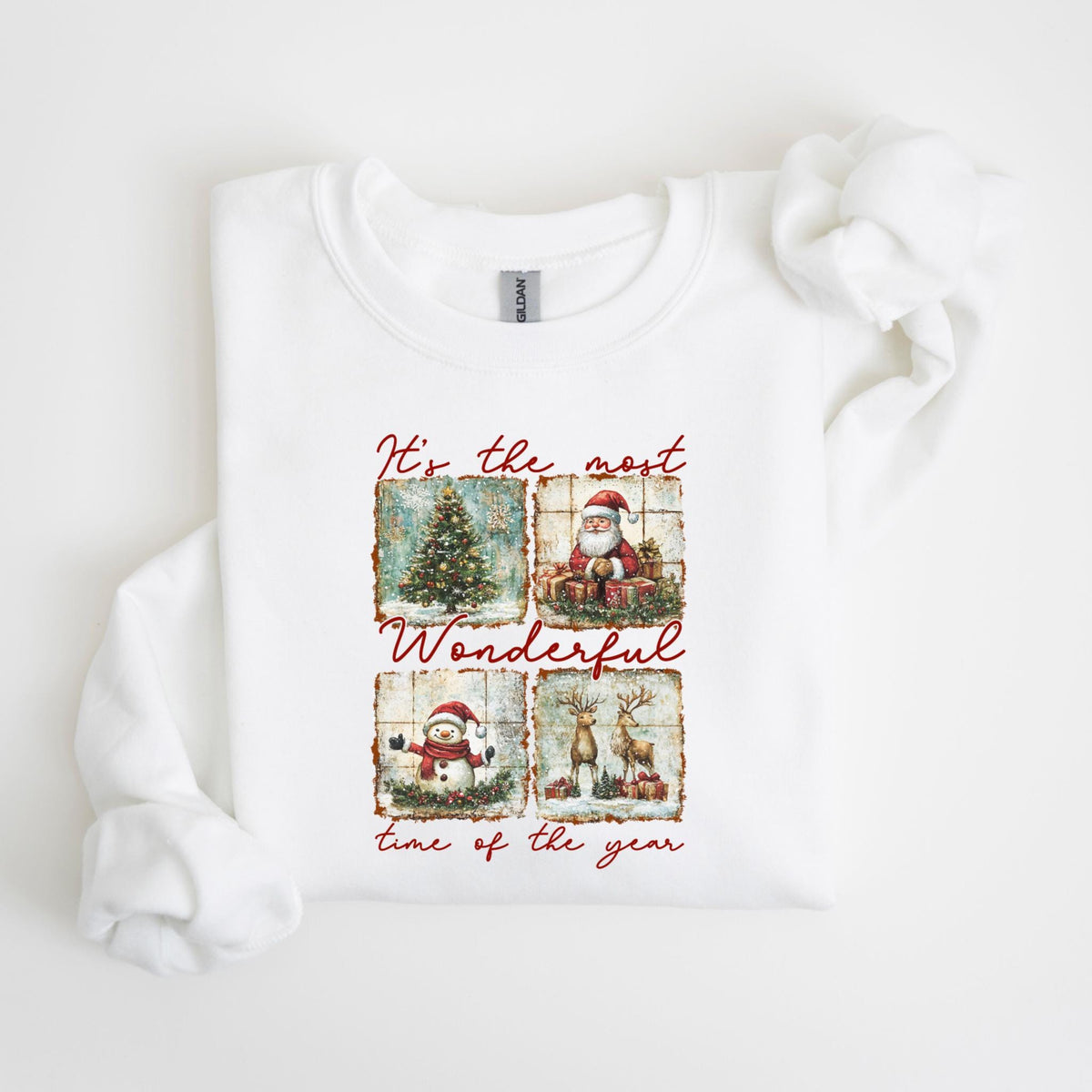 May include: White crewneck sweatshirt with a festive design. The design features four squares with Christmas-themed illustrations: a decorated tree, Santa Claus, a snowman, and reindeer. The text "It's the most Wonderful time of the year" is written in red.