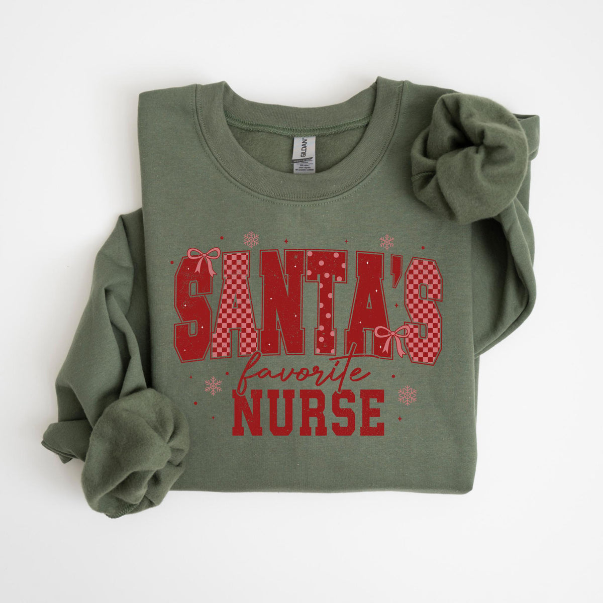 May include: An olive green sweatshirt with the text "SANTA'S favorite NURSE" in red. The text has a checkered pattern and is decorated with bows and snowflakes. The sweatshirt is folded.