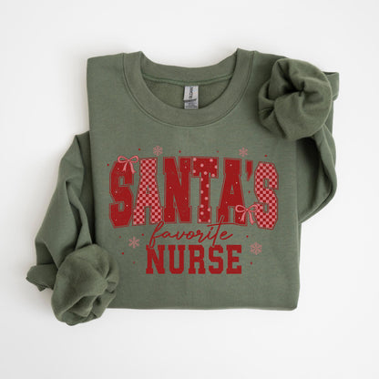 May include: An olive green sweatshirt with the text "SANTA'S favorite NURSE" in red. The text has a checkered pattern and is decorated with bows and snowflakes. The sweatshirt is folded.