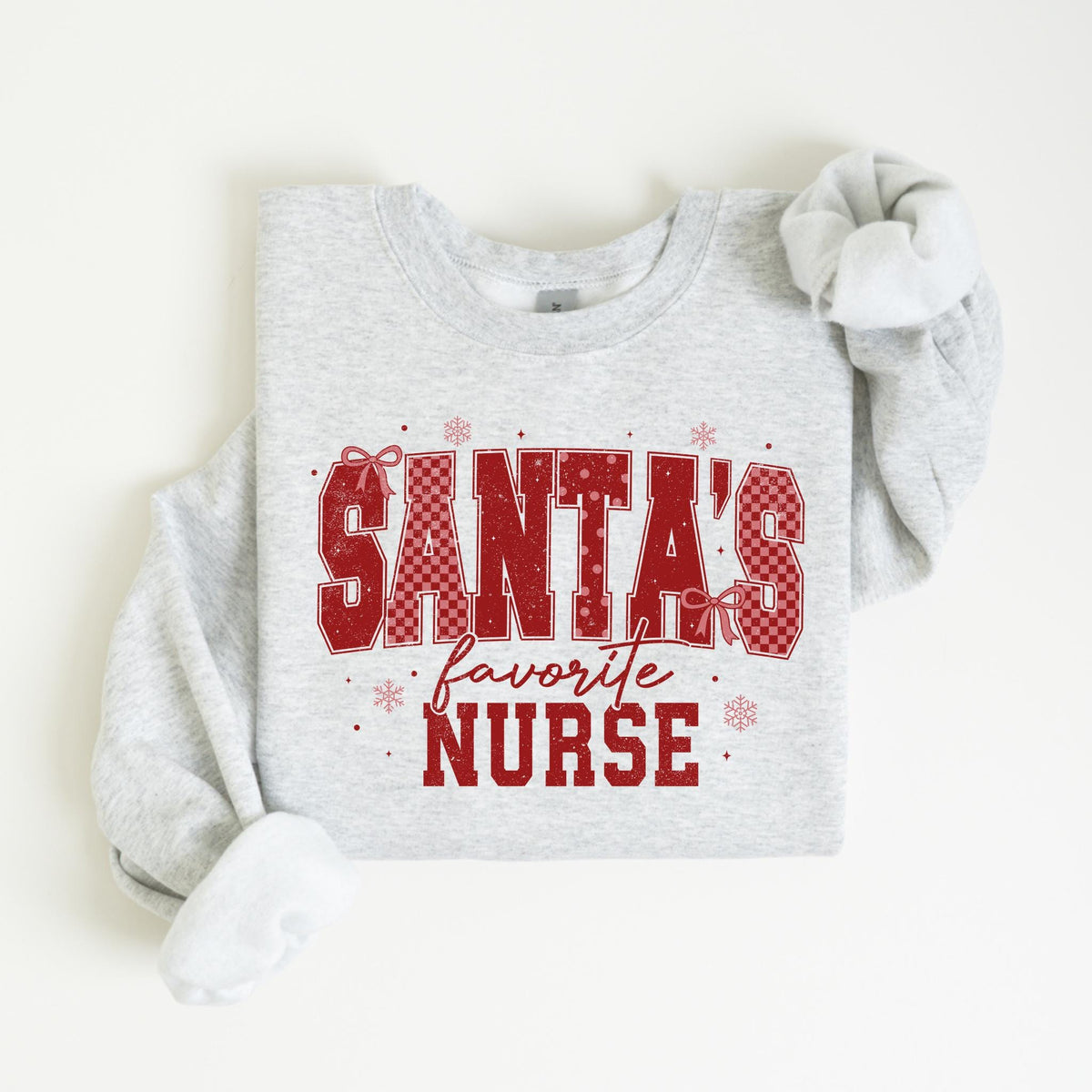 May include: A light gray sweatshirt with the text "SANTA'S favorite NURSE" in red. The text has a plaid pattern and is decorated with snowflakes and bows. The sweatshirt has a crew neck and long sleeves.