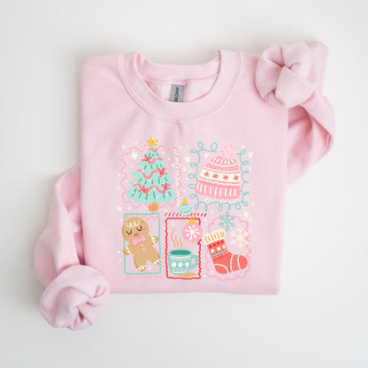 May include: A light pink sweatshirt with a festive graphic. The graphic includes a Christmas tree, a gingerbread man, a mug of hot cocoa, a stocking, and a winter hat, all in a whimsical style. The design is outlined with a light blue border.