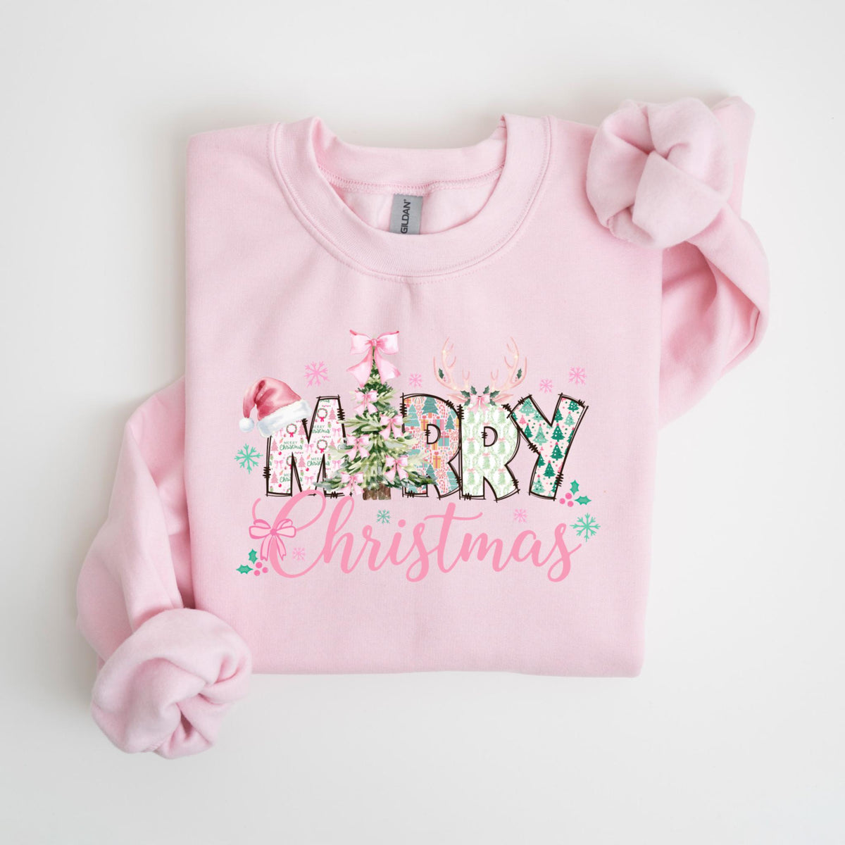 May include: A light pink sweatshirt with the words "Merry Christmas" in a decorative font. The word "Merry" features a Christmas tree, snowflakes, and a Santa hat. The word "Christmas" is in a cursive font with floral accents.