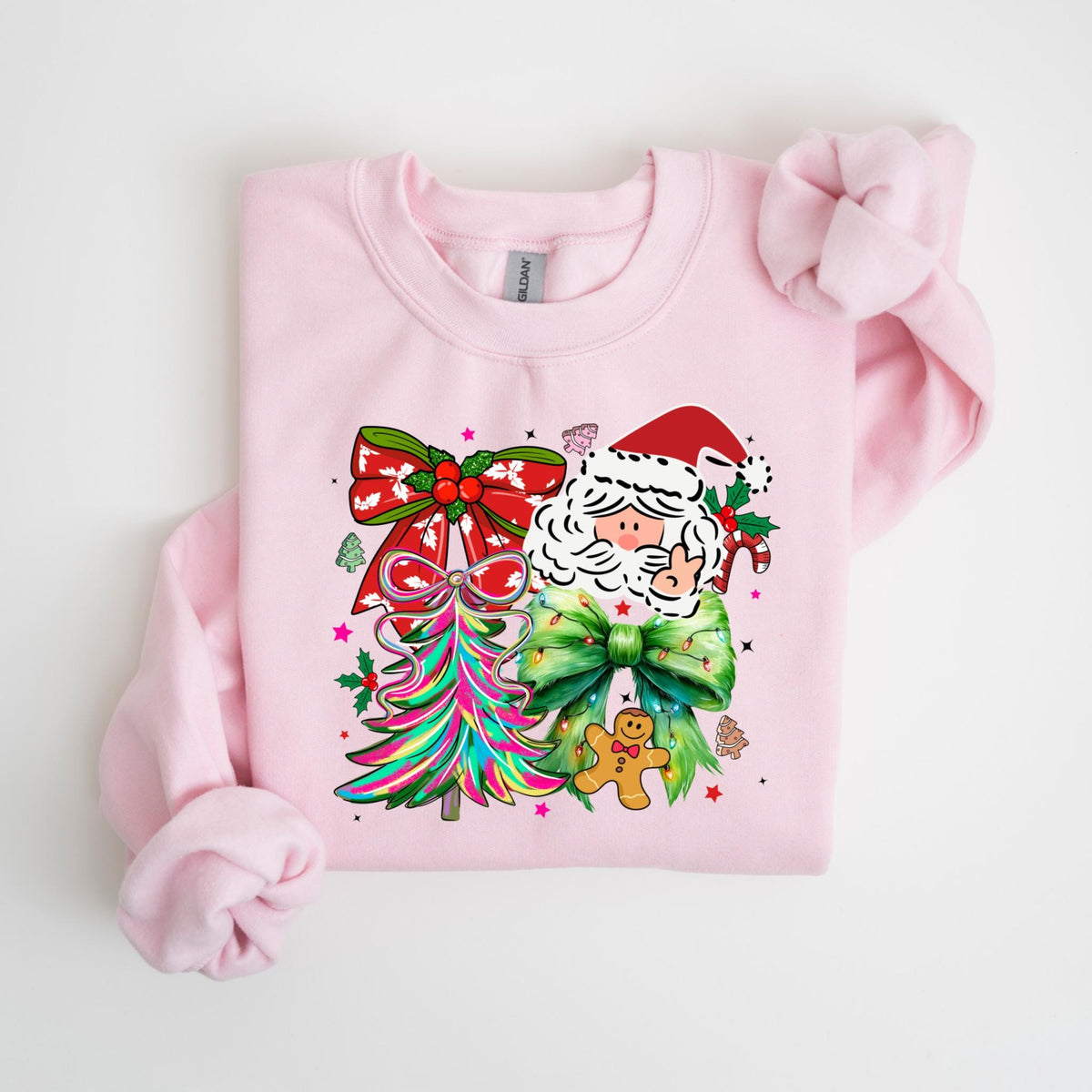 May include: A light pink sweatshirt featuring a colorful Christmas design. The graphic includes a Santa Claus face, a Christmas tree, and bows. A gingerbread man and candy canes are also part of the design.