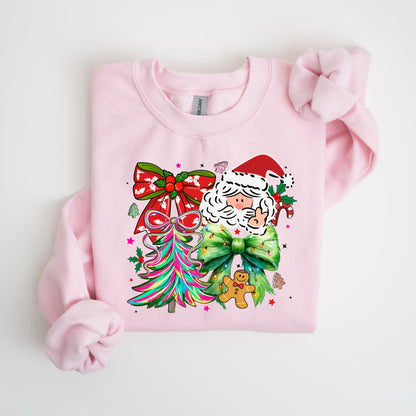 May include: A light pink sweatshirt featuring a colorful Christmas design. The graphic includes a Santa Claus face, a Christmas tree, and bows. A gingerbread man and candy canes are also part of the design.