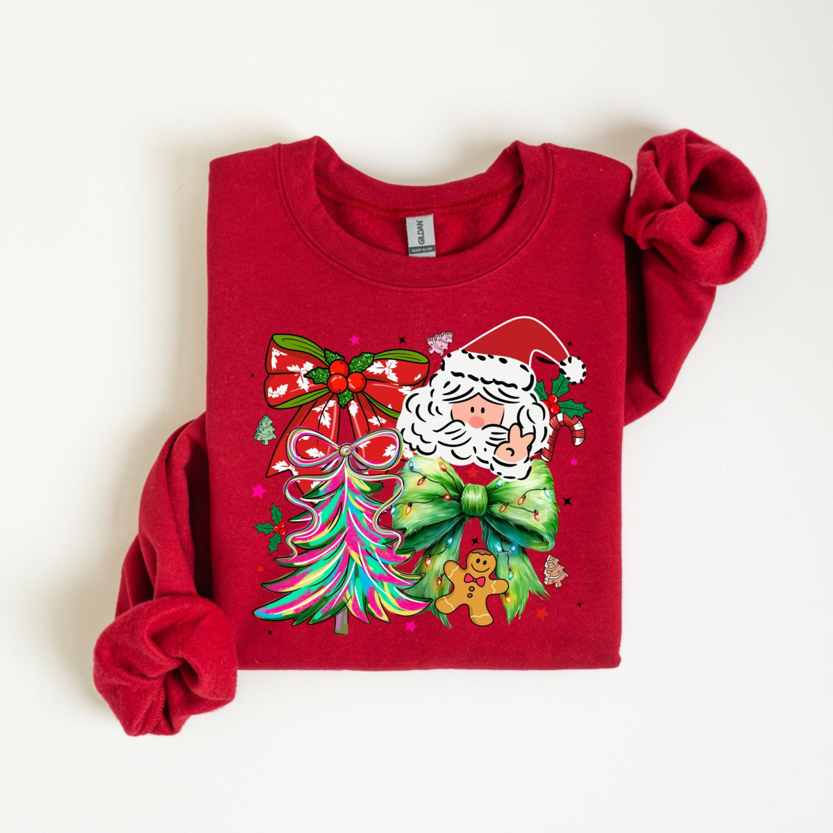 May include: Red crewneck sweatshirt featuring a Christmas-themed graphic. The design includes Santa Claus, colorful bows, a Christmas tree, and a gingerbread man. The sweatshirt is folded, with the sleeves visible.