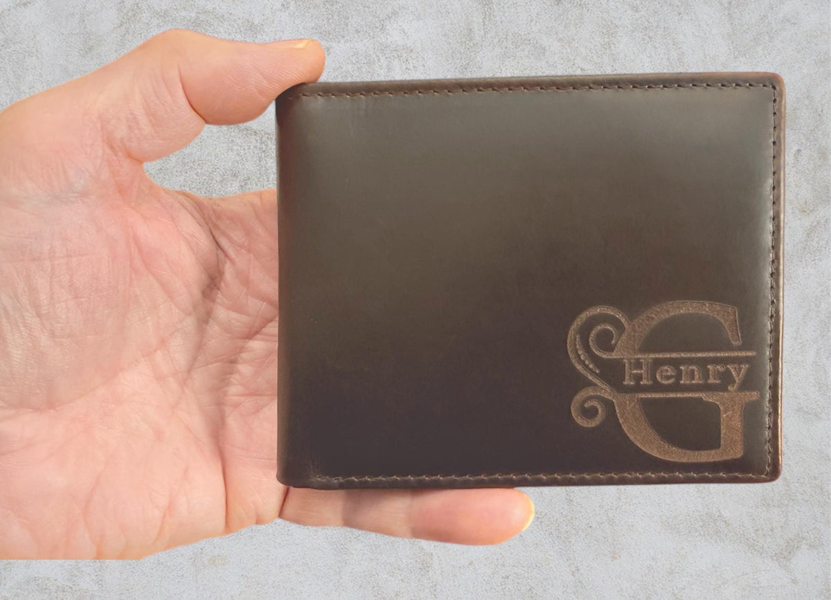 May include: A brown leather wallet with the name "Henry" engraved in a decorative font. The wallet is rectangular and appears to be new. The wallet is held in a hand.