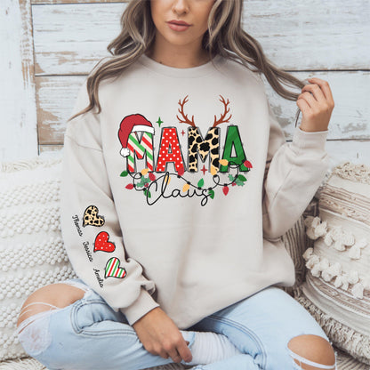 May include: Beige sweatshirt with a festive "Mama Claus" design. The design features a Santa hat, reindeer antlers, and the word "Mama" in various patterns. The word "Claus" is written in cursive. The left sleeve has heart graphics with names.