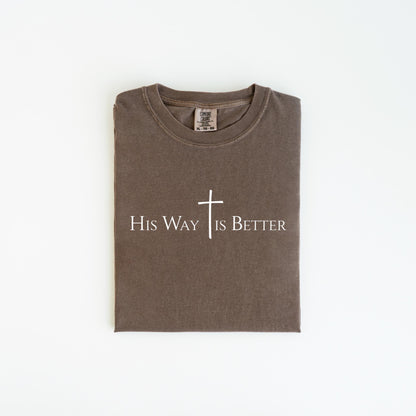 May include: A folded, brown t-shirt with the text "His Way Is Better" and a white cross graphic. The shirt is made of a soft material and has a crew neck.