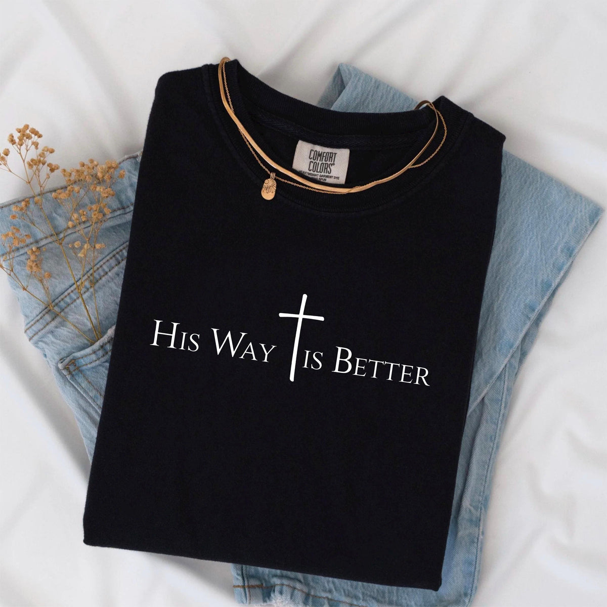 May include: Black t-shirt with the text "His Way Is Better" and a cross graphic. The shirt is paired with a gold necklace and light blue denim jeans. The shirt is made by Comfort Colors.