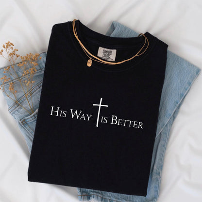 May include: Black t-shirt with the text "His Way Is Better" and a cross graphic. The shirt is paired with a gold necklace and light blue denim jeans. The shirt is made by Comfort Colors.