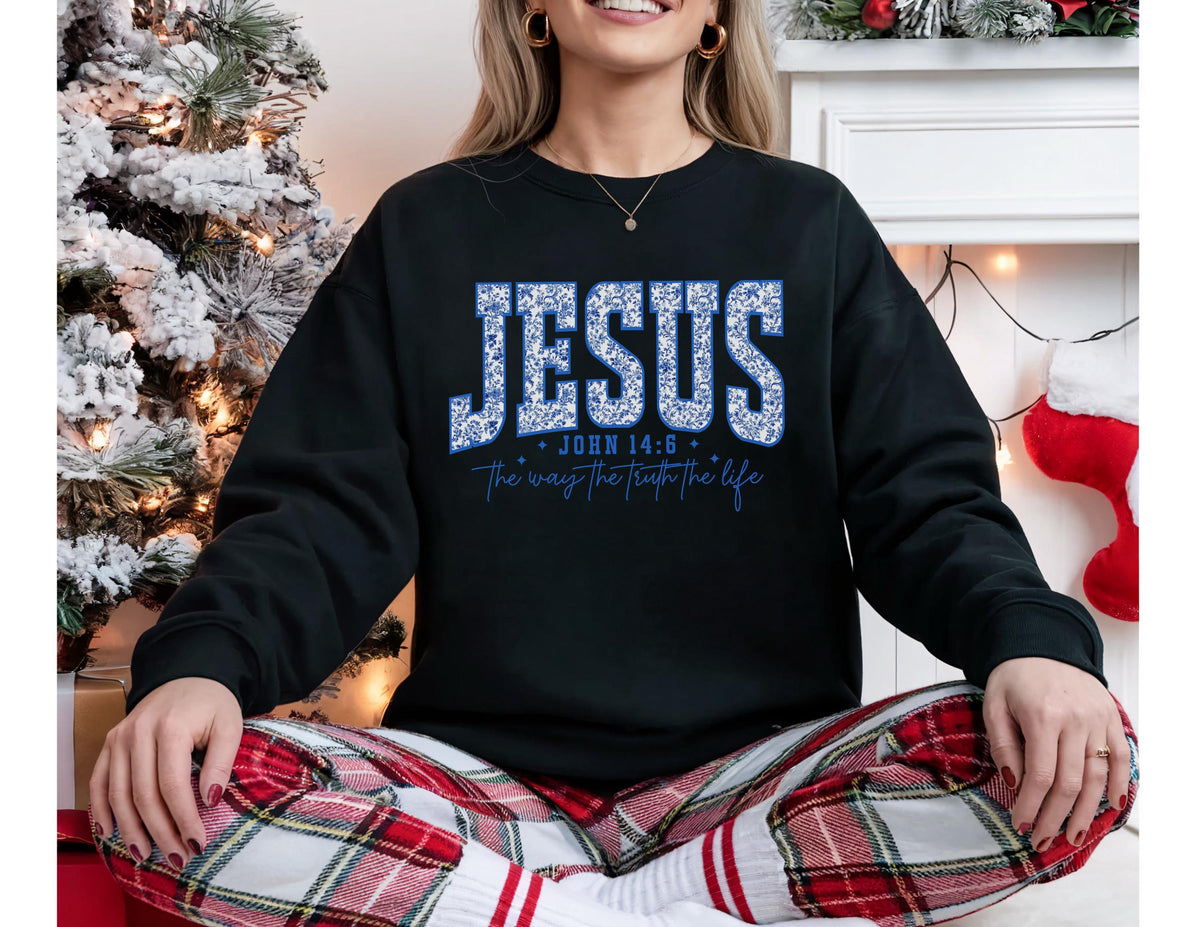 May include: Black sweatshirt with the word "JESUS" in blue floral lettering. Below the word "JESUS" is the text "John 14:6" and "the way the truth the life" in a script font. The sweatshirt is part of a religious apparel collection.