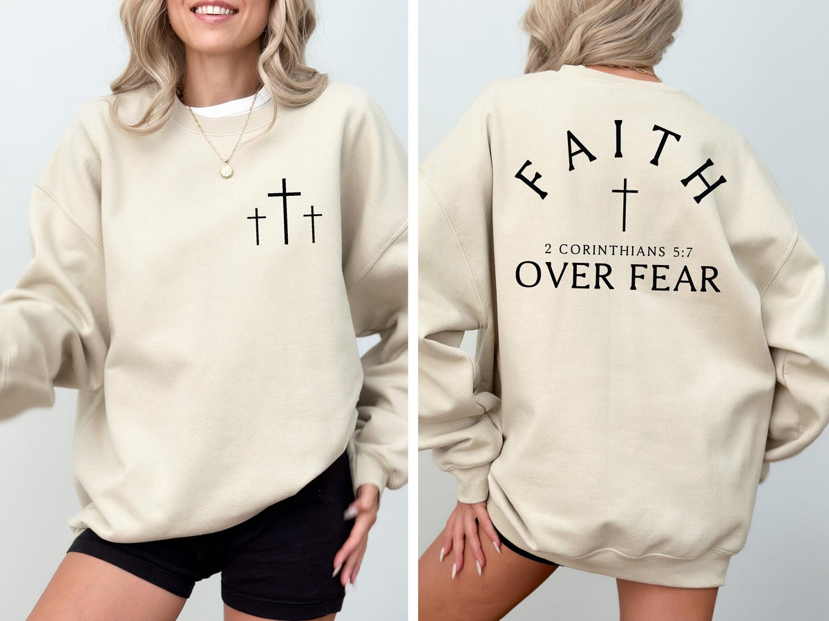 May include: Beige sweatshirt with three black crosses on the front. The back of the sweatshirt features the word "FAITH" arched above a cross, with "2 Corinthians 5:7 OVER FEAR" printed below. A casual, comfortable garment.