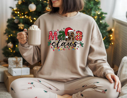May include: A beige sweatshirt with the text "Mama Claus" in a festive design. The letters are decorated with red hearts, green plaid, and leopard print. A Santa hat tops the "M". The sweatshirt is paired with matching pajama pants.