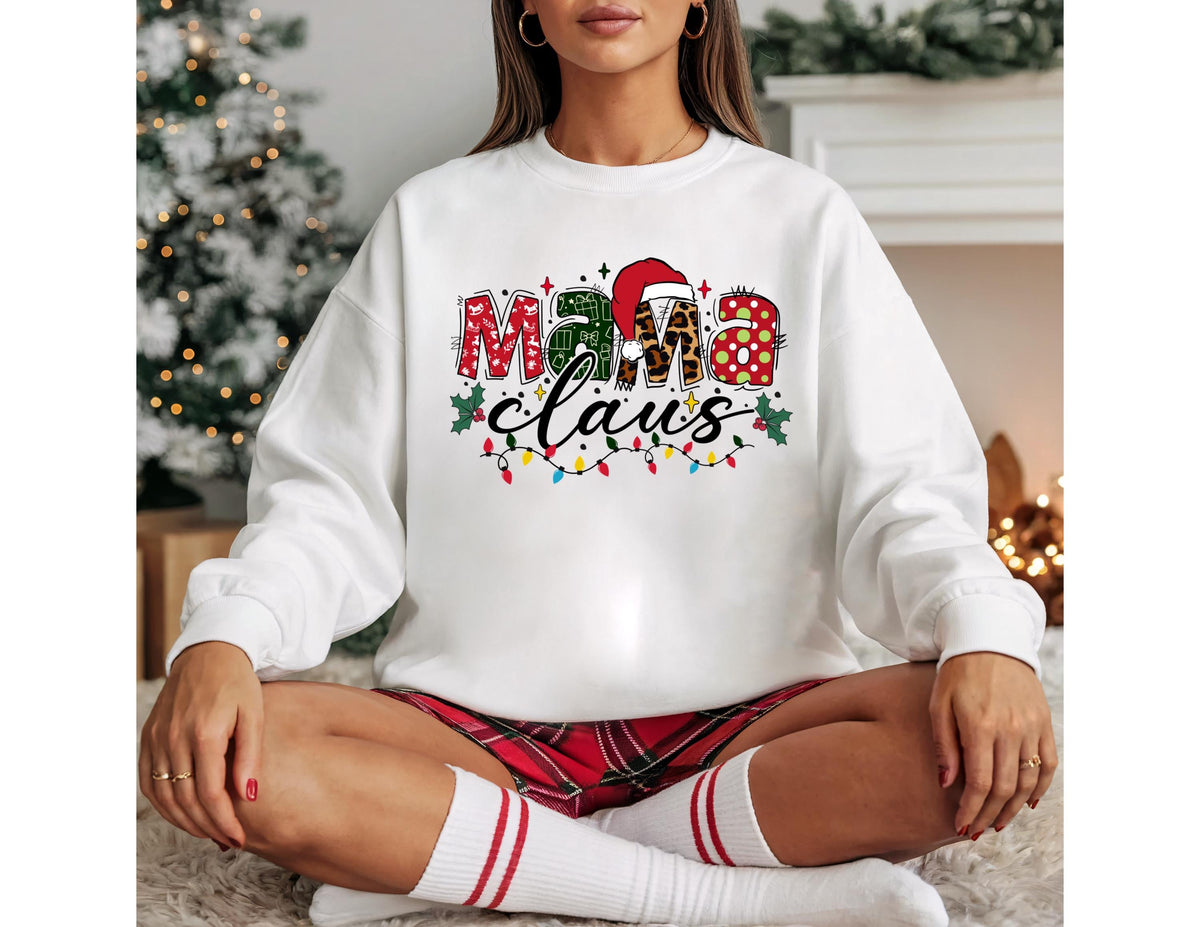 May include: White long-sleeve sweatshirt with the text "Mama Claus" in a festive design. The text features red, green, and leopard print elements, with a Santa hat on the letter "M". A string of Christmas lights is below the text.