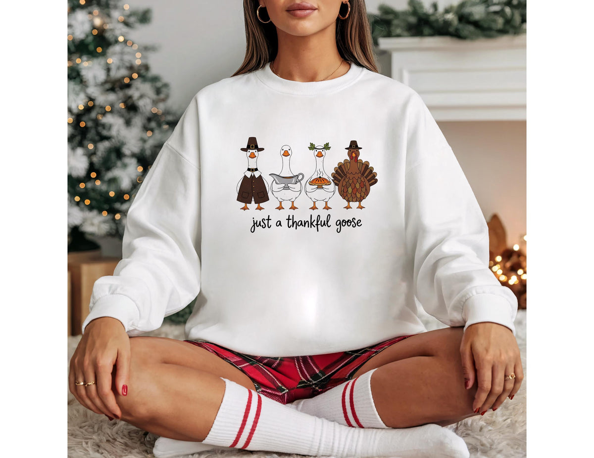 May include: White sweatshirt featuring a graphic of four cartoon geese and a turkey, each wearing festive attire. The text "just a thankful goose" is printed below the characters. The sweatshirt is a long-sleeved, crew neck style.