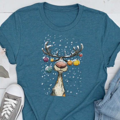 May include: Teal t-shirt featuring a cartoon reindeer with large antlers decorated with colorful ornaments. The reindeer has a large red nose and is surrounded by falling snowflakes. The shirt is a casual, festive design.