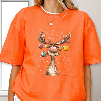 May include: Orange t-shirt featuring a cartoon reindeer with antlers adorned with colorful ornaments. The reindeer has a large nose and is set against a snowy background. The shirt is a vibrant orange color.