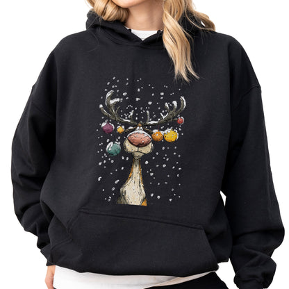 May include: A black hooded sweatshirt featuring a graphic print of a reindeer with a large pink nose and antlers decorated with colorful Christmas ornaments. The reindeer is depicted in a snowy setting with white snowflakes falling around it.
