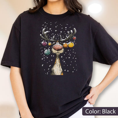 May include: A black short-sleeve t-shirt featuring a graphic illustration of a reindeer with a large nose and antlers decorated with colorful hanging ornaments. The reindeer is depicted against a background of falling white snow.