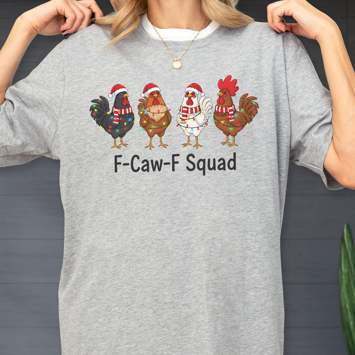 May include: A light gray crew neck sweatshirt featuring four cartoon roosters wearing Santa hats and Christmas lights. The text "F-Caw-F Squad" is printed below the roosters. The sweatshirt has a white collar.