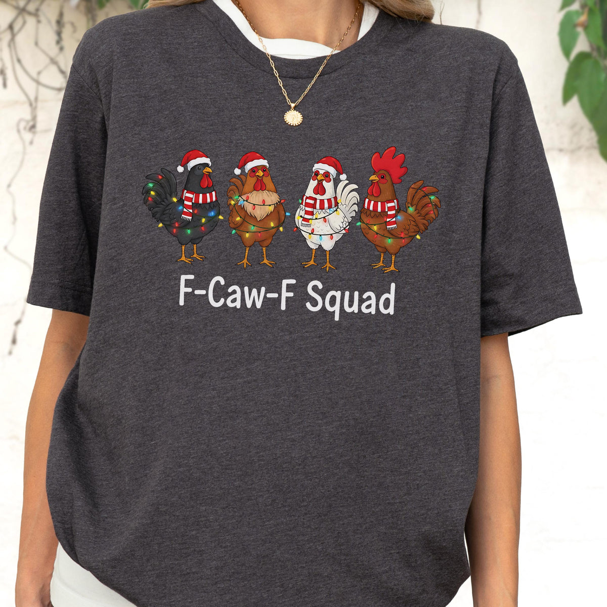 May include: Dark gray t-shirt featuring four cartoon chickens decorated with Christmas lights and Santa hats. The text "F-Caw-F Squad" is printed in white below the chickens. The shirt has a crew neck and short sleeves.