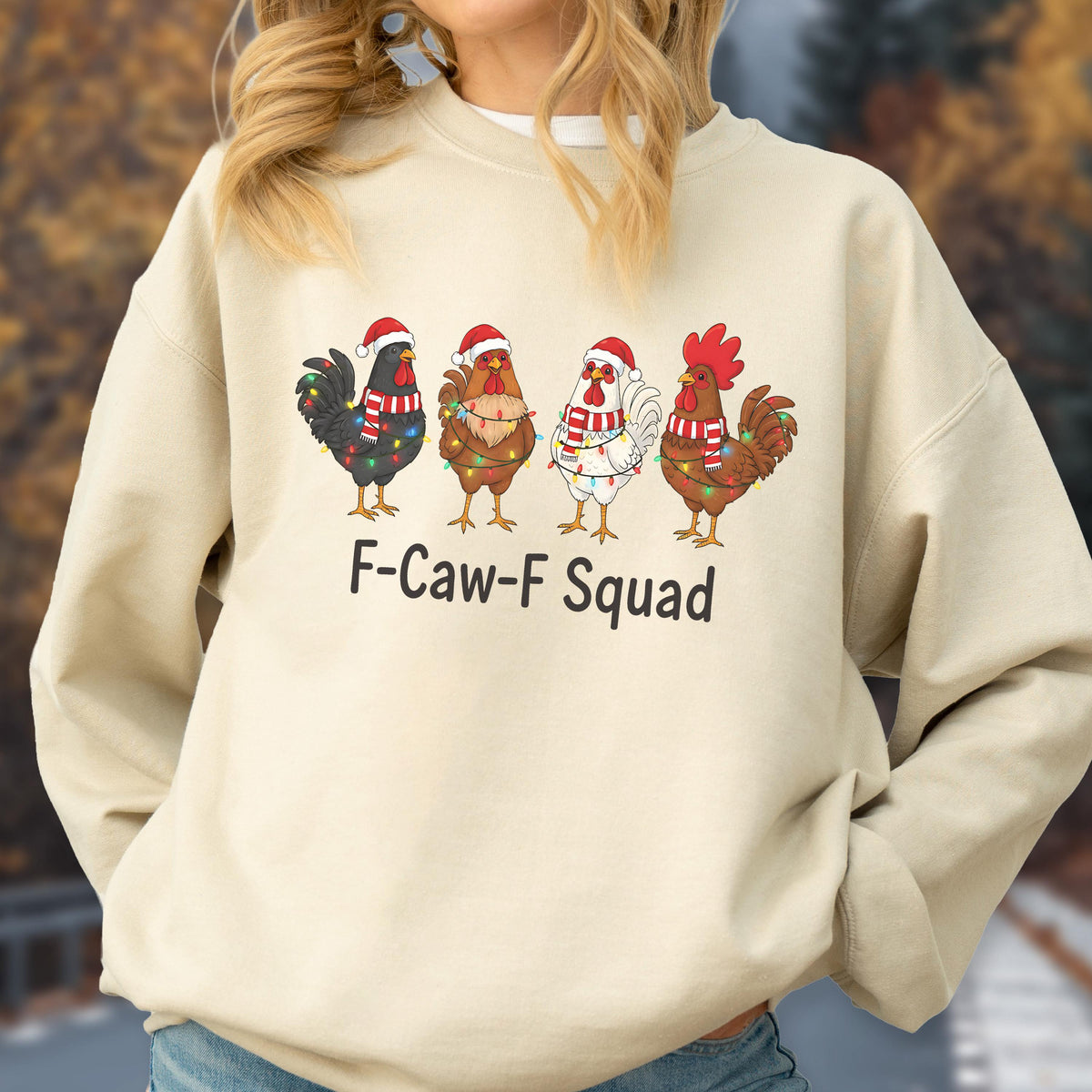 May include: A beige sweatshirt featuring four cartoon chickens wearing Santa hats and Christmas lights. The text "F-Caw-F Squad" is printed below the chickens. The chickens are in various colors, including black, brown, and white.