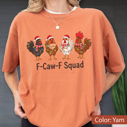 May include: Orange-colored t-shirt with the text "F-Caw-F Squad." The shirt features a graphic of four chickens wearing Santa hats and scarves, decorated with Christmas lights. The shirt's color is "Yam."
