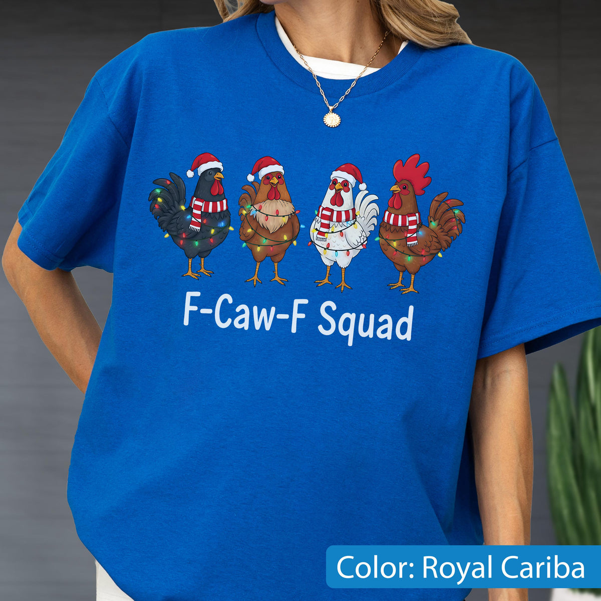 May include: Royal Cariba blue t-shirt featuring a graphic of four cartoon chickens wearing Santa hats and scarves, adorned with Christmas lights. The text "F-Caw-F Squad" is printed below the chickens.