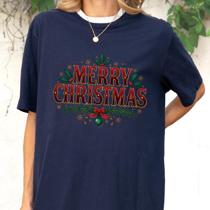May include: A navy blue short-sleeve t-shirt featuring the text Merry Christmas in a red and gold font. The design is decorated with green holly leaves, red berries, pine branches, a red bow, and a green ornament, all accented by gold stars.