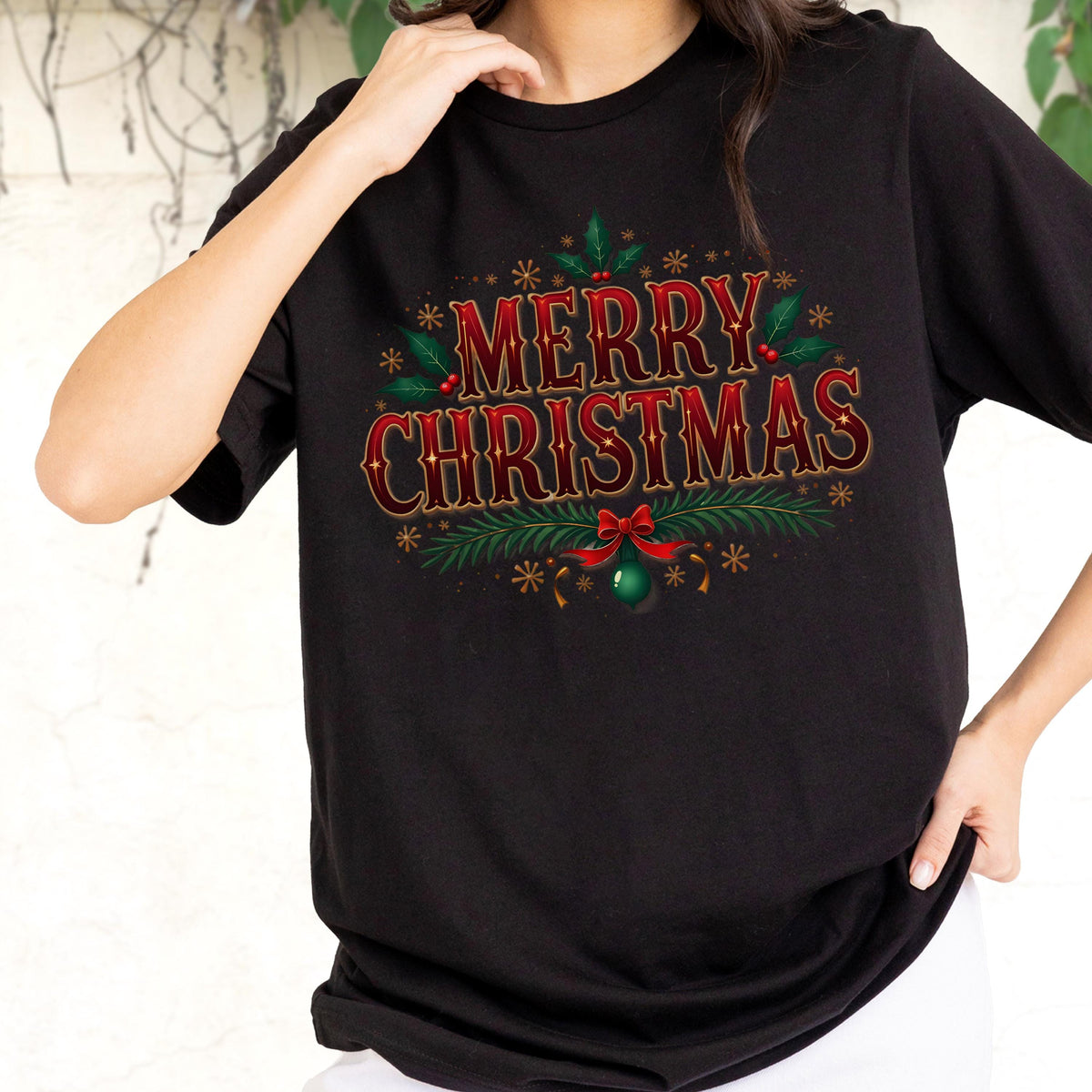 May include: A black short-sleeved t-shirt featuring the text MERRY CHRISTMAS in red and gold lettering. The design includes green holly leaves, red berries, pine branches, a red bow, and a green ornament, accented by small gold star-like shapes.