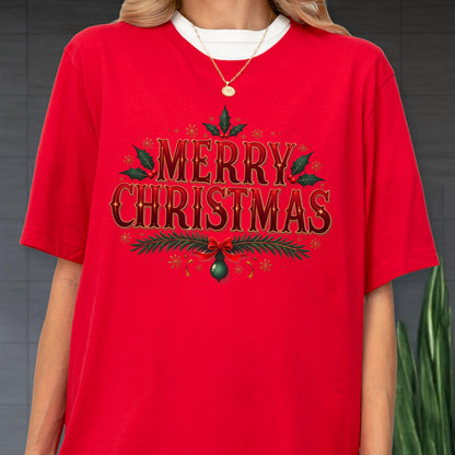 May include: A bright red short-sleeved t-shirt featuring the text MERRY CHRISTMAS in a decorative gold and dark red font. The design is accented with green holly leaves, red berries, pine branches, a red bow, and small gold starbursts.