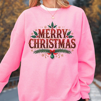 May include: A pink sweatshirt with the words "MERRY CHRISTMAS" in a decorative, festive font. The text is in red and gold, surrounded by holly leaves, snowflakes, and a green ornament with a red bow.